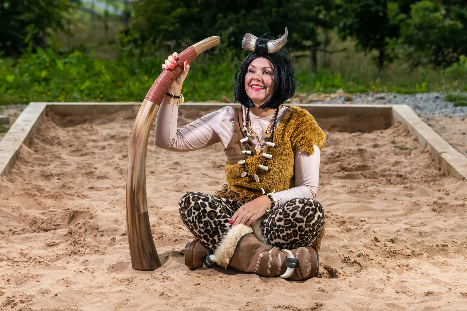 A woman in a costume is sitting in the sand holding a boomerang.