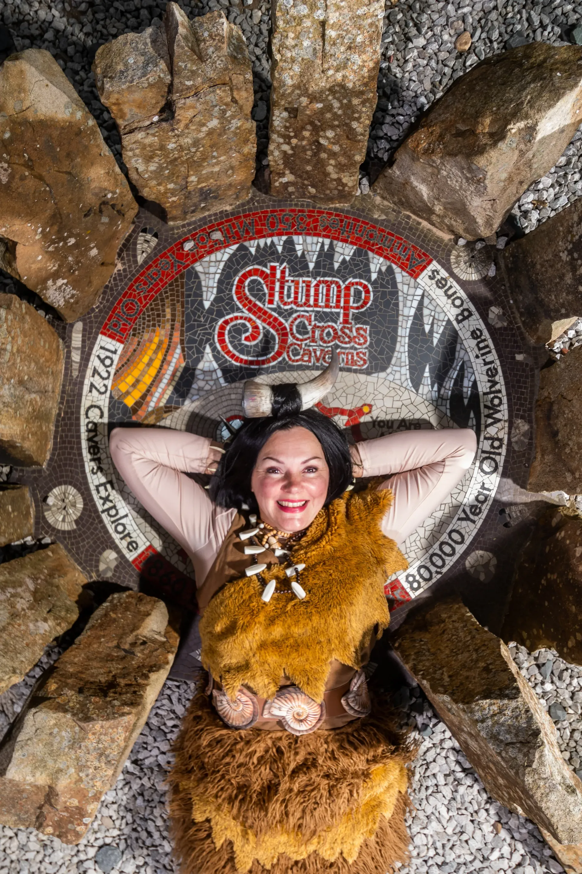 A woman in a caveman costume is laying on a pile of rocks.