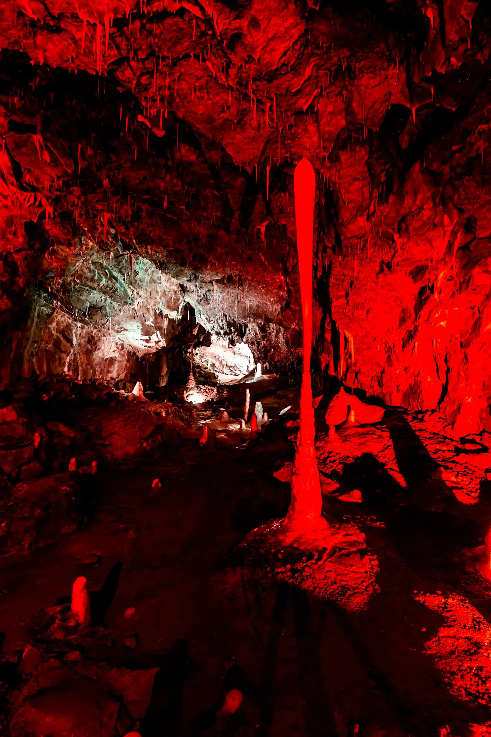 A cave with red lights on the walls and a red stream of lava coming out of it.