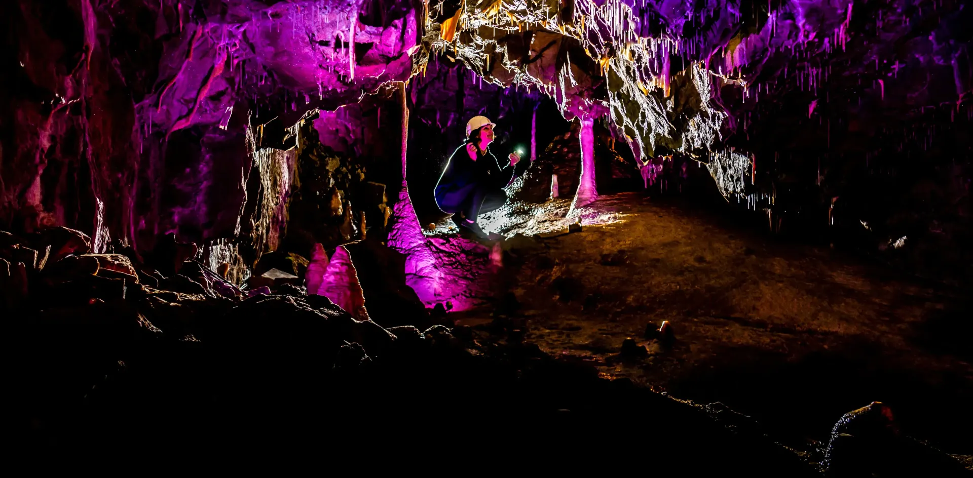 A person is sitting in a cave surrounded by purple lights.