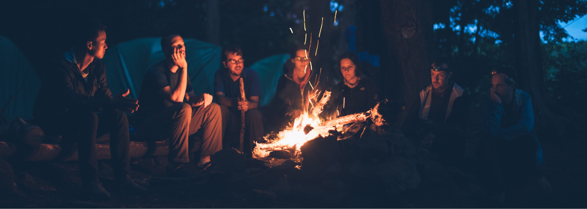 Picture of a group of people in outdoor gear chatting around a fire.