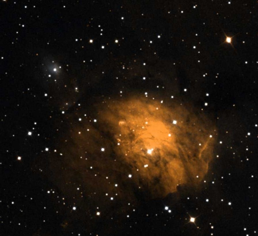 Orange nebula with a bright core surrounded by dark dust and scattered stars.