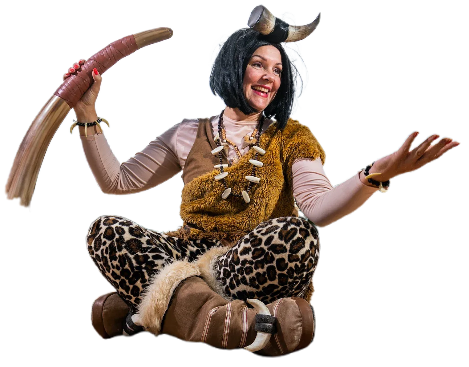 A woman in a caveman costume is sitting on the ground holding a large horn.