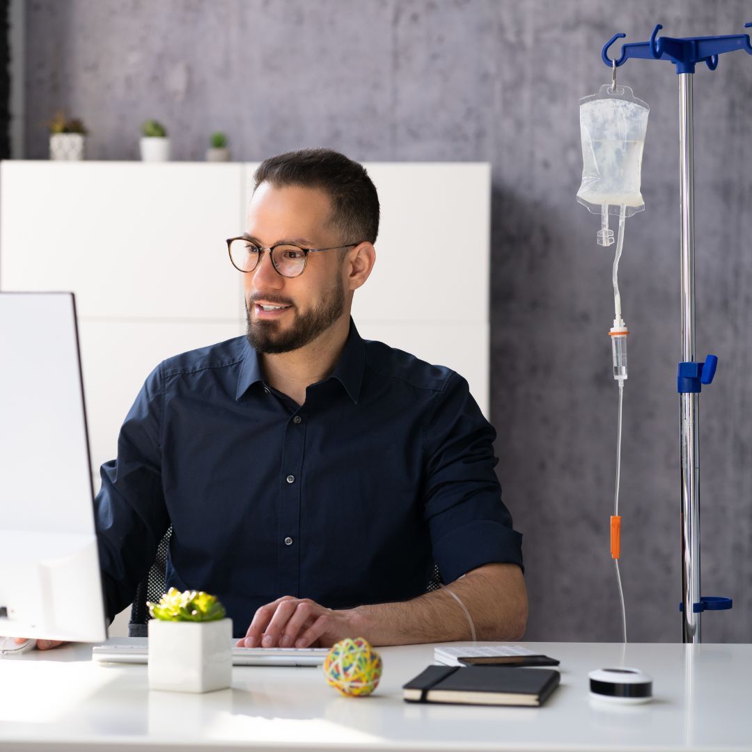 A man wearing glasses is sitting at a desk in front of a computer