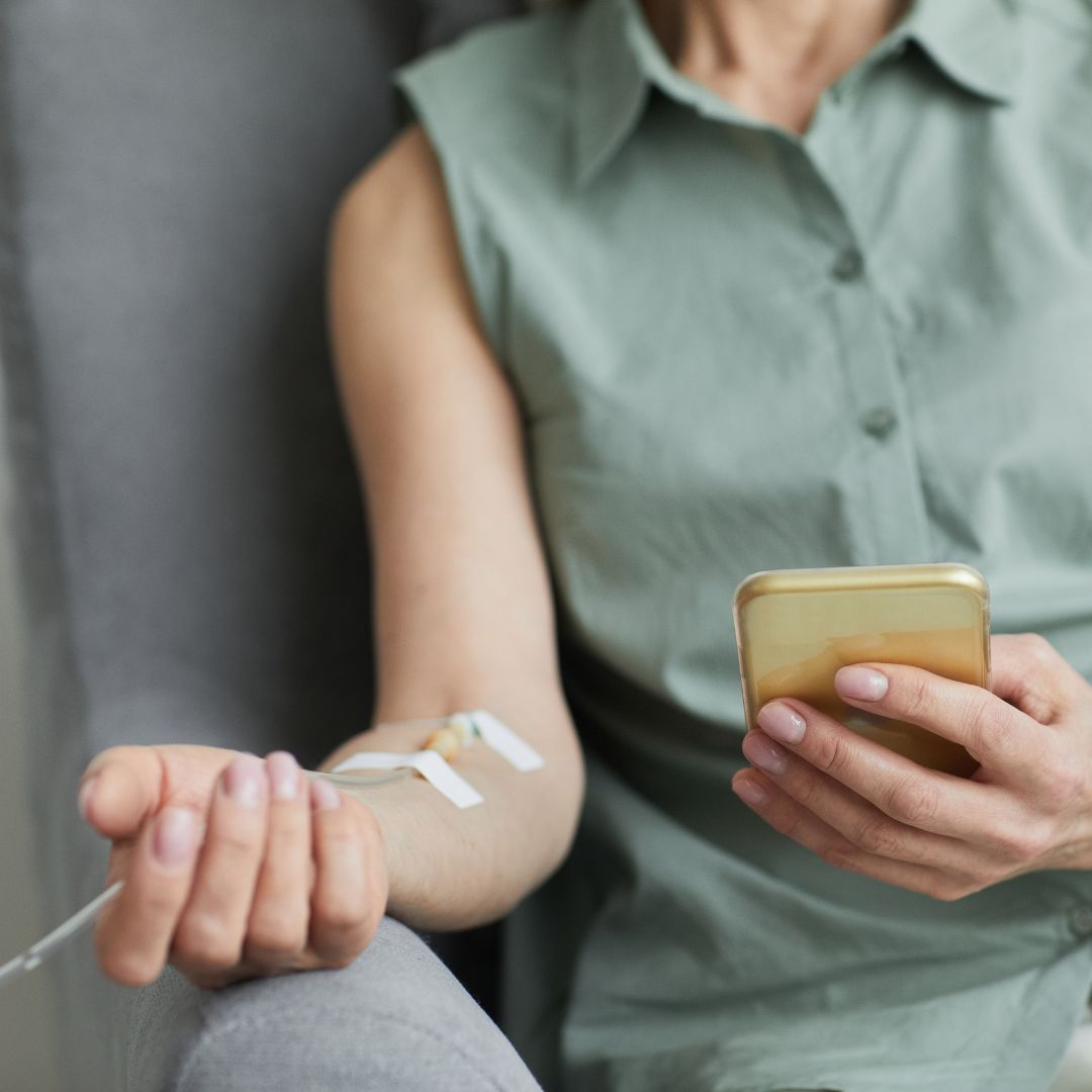 A woman is sitting in a chair holding a cell phone and a syringe in her arm