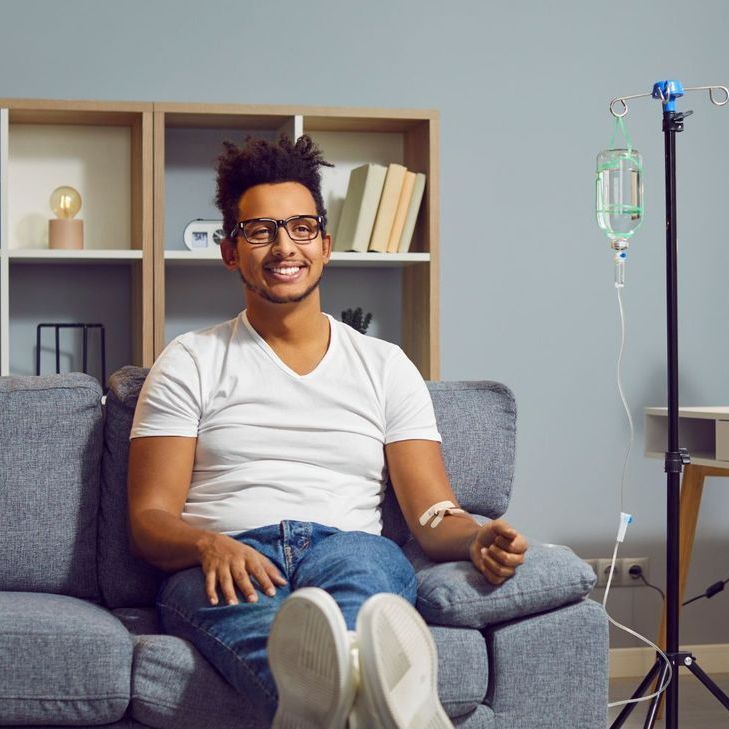 A man is sitting on a couch with an iv in his arm.