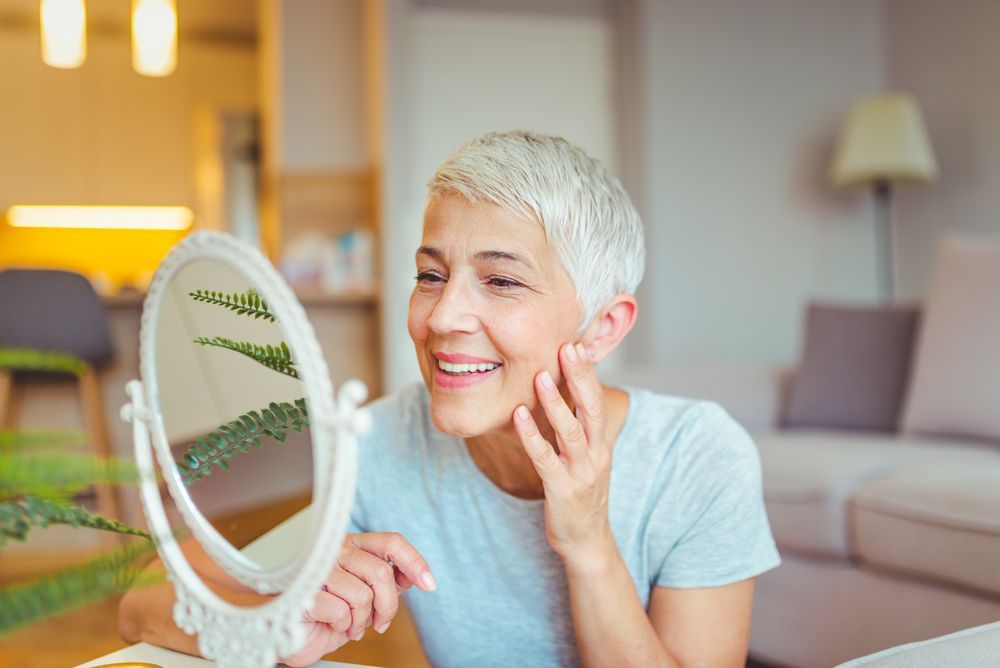 A woman is looking at her face in a mirror.