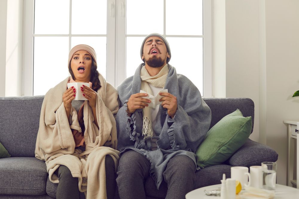 A man and a woman are sitting on a couch covered in blankets.