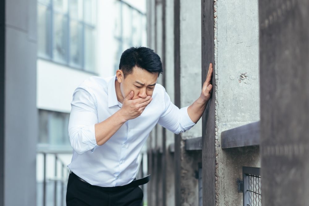 A man is leaning against a wall and covering his mouth with his hand.