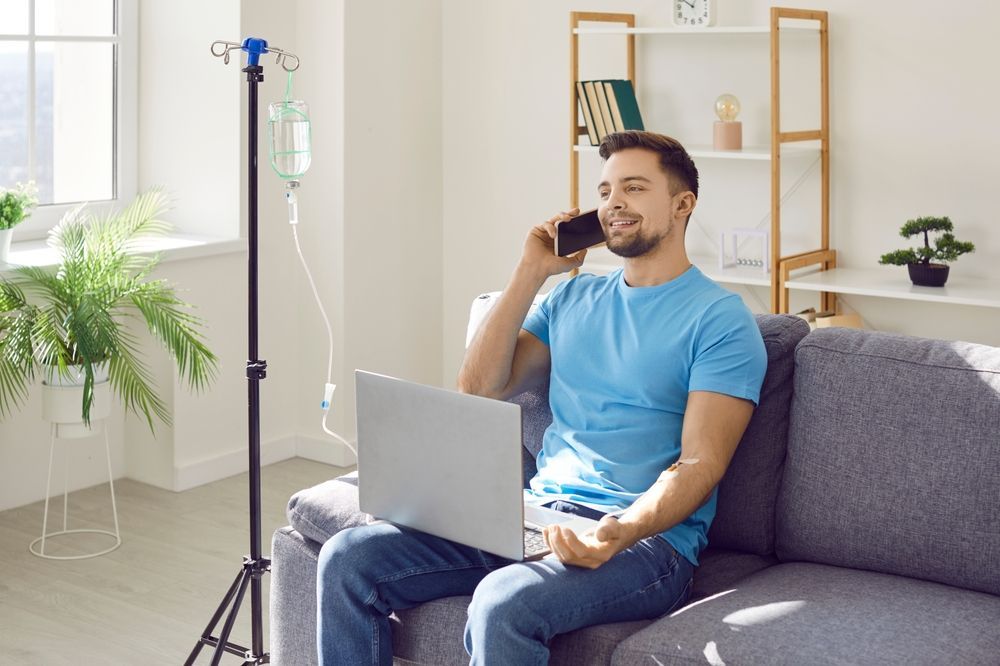 A man is sitting on a couch with a laptop and talking on a cell phone.