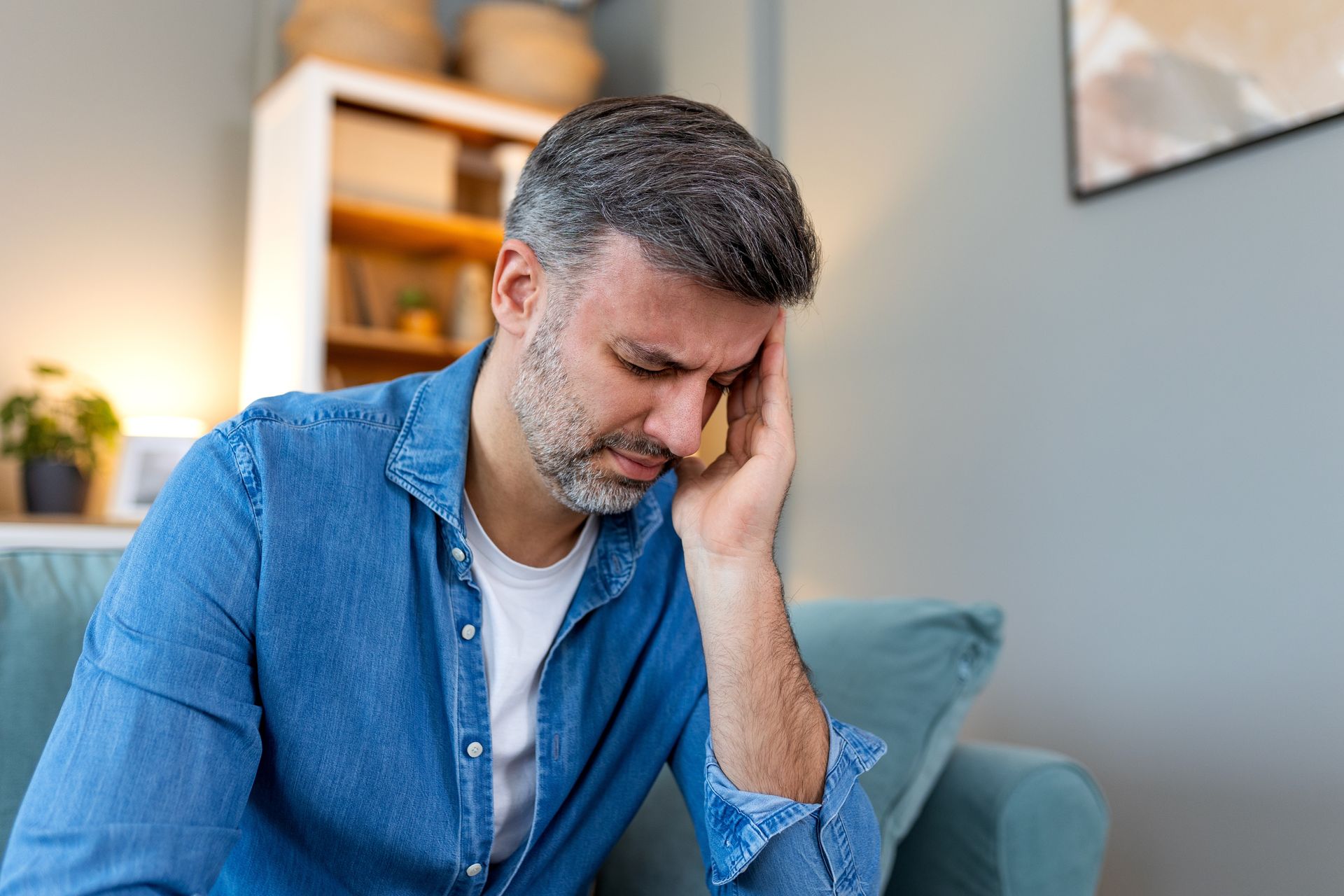 A man is sitting on a couch with his hand on his head.