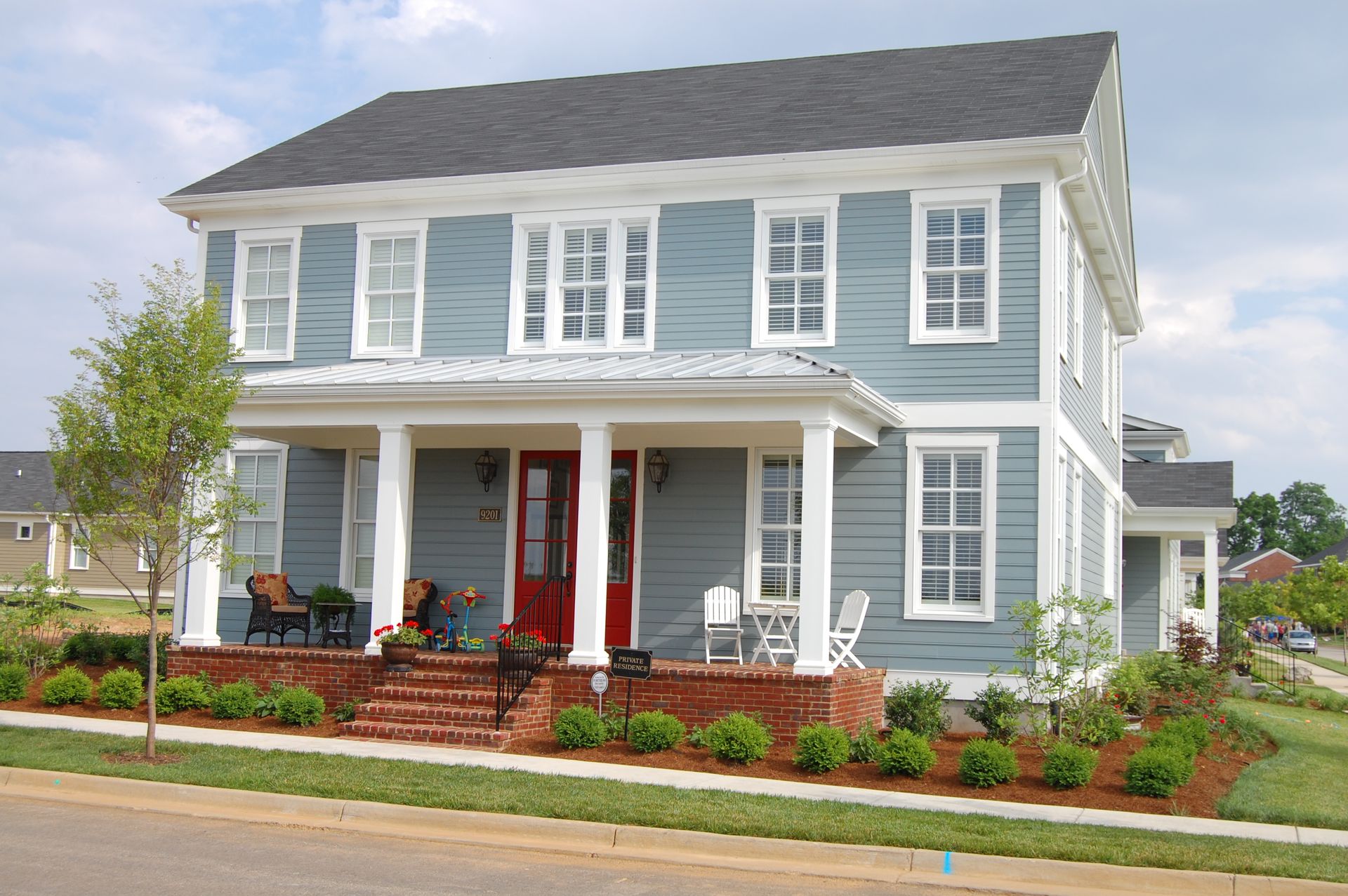 A large gray house with a black roof is sitting on top of a lush green field.