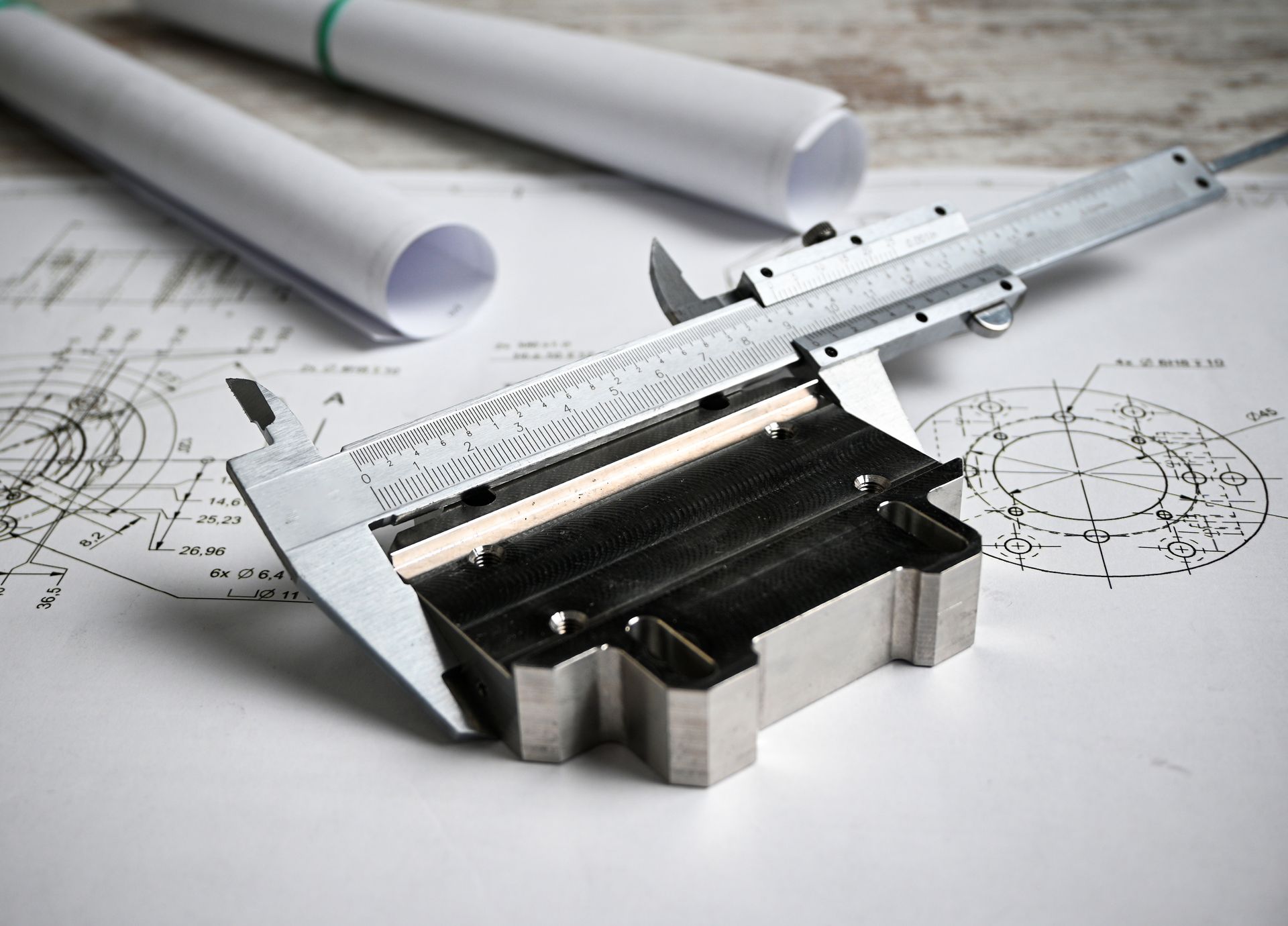 Silver caliper on technical drawings beside rolled blueprints