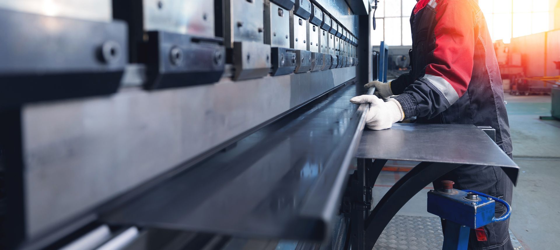 Worker operating a large industrial machine in a factory, wearing gloves and red safety gear