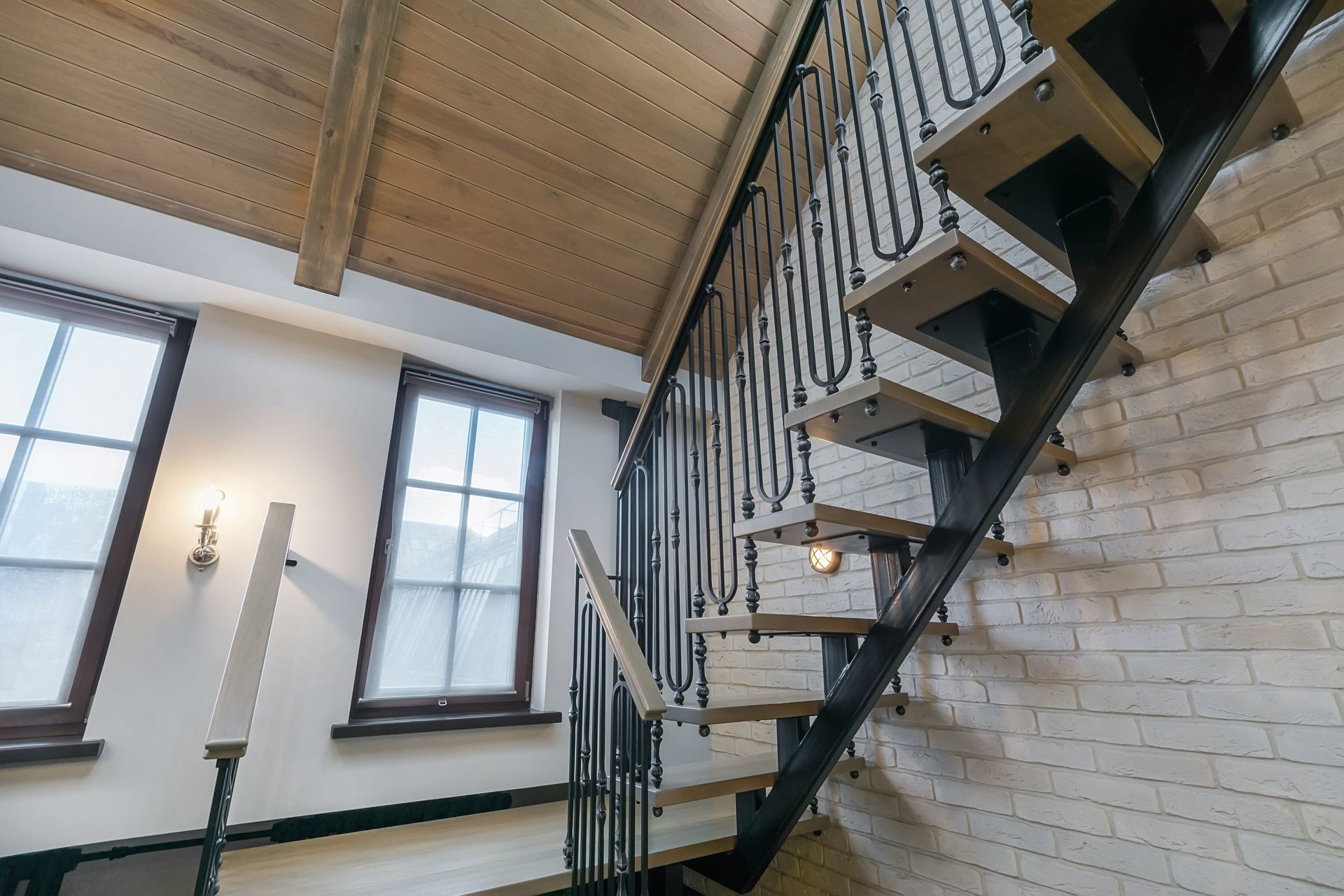 Modern staircase with black railing in a bright room with exposed brick and wooden ceiling