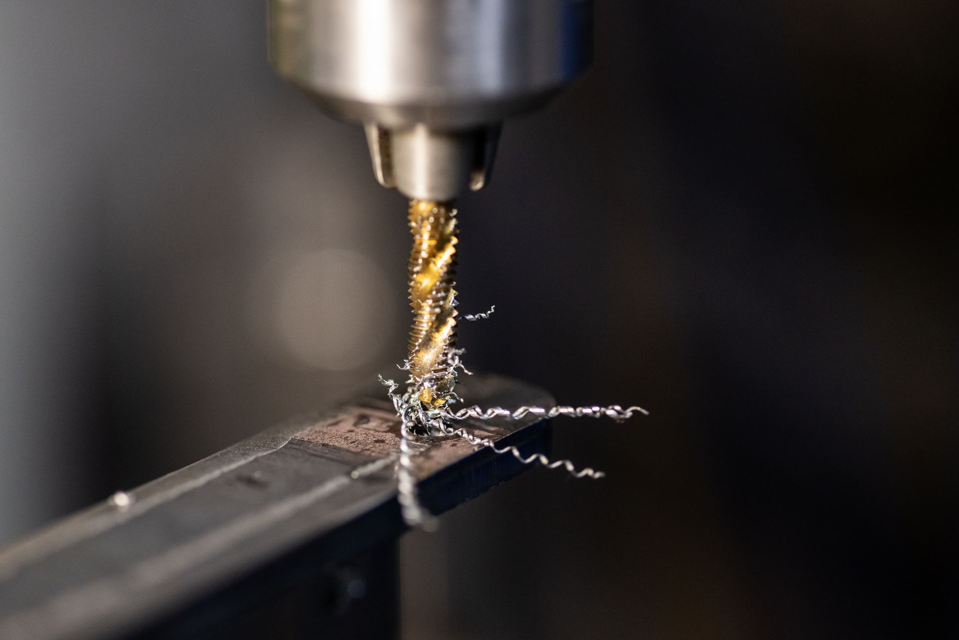 Close-up of a drill bit cutting into metal, with shavings curling off the workpiece.