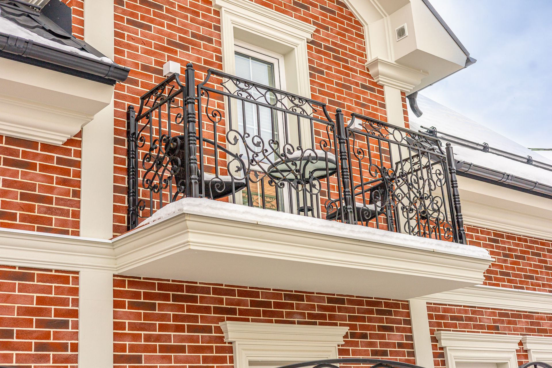 Brick house balcony with ornate black wrought-iron railing above a white-trimmed entrance
