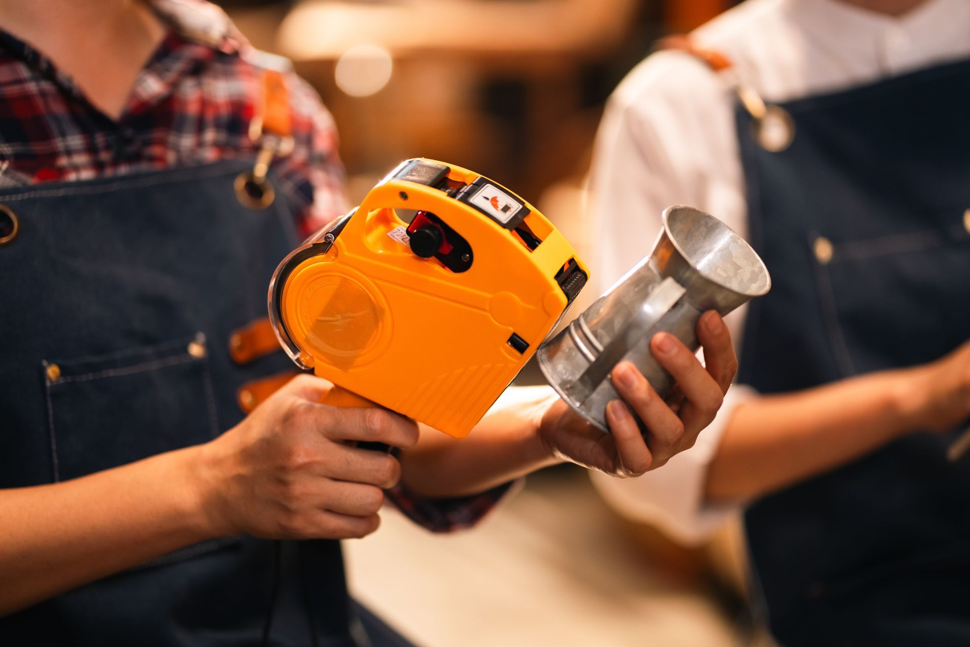 Person holding an orange drill and a metal cup in a workshop setting