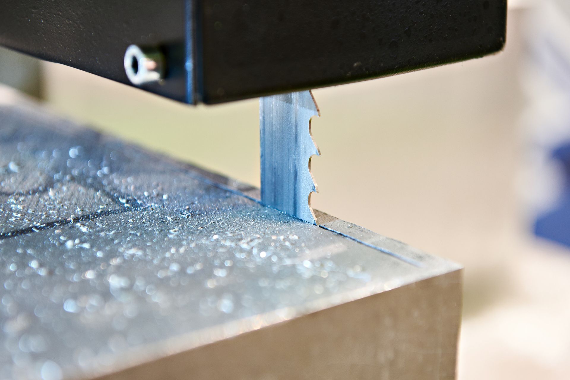 Bandsaw cutting metal with blue blade and metal shavings on the surface