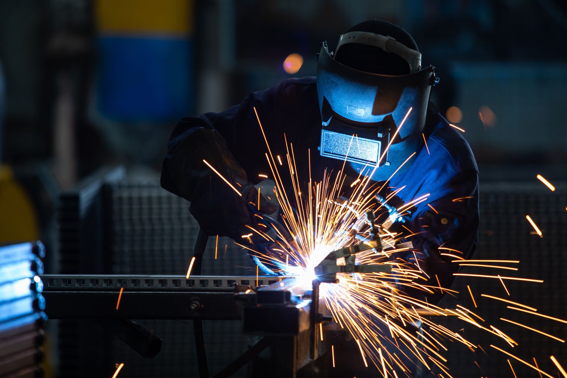 Welder in blue protective gear sparks metal in a dim workshop