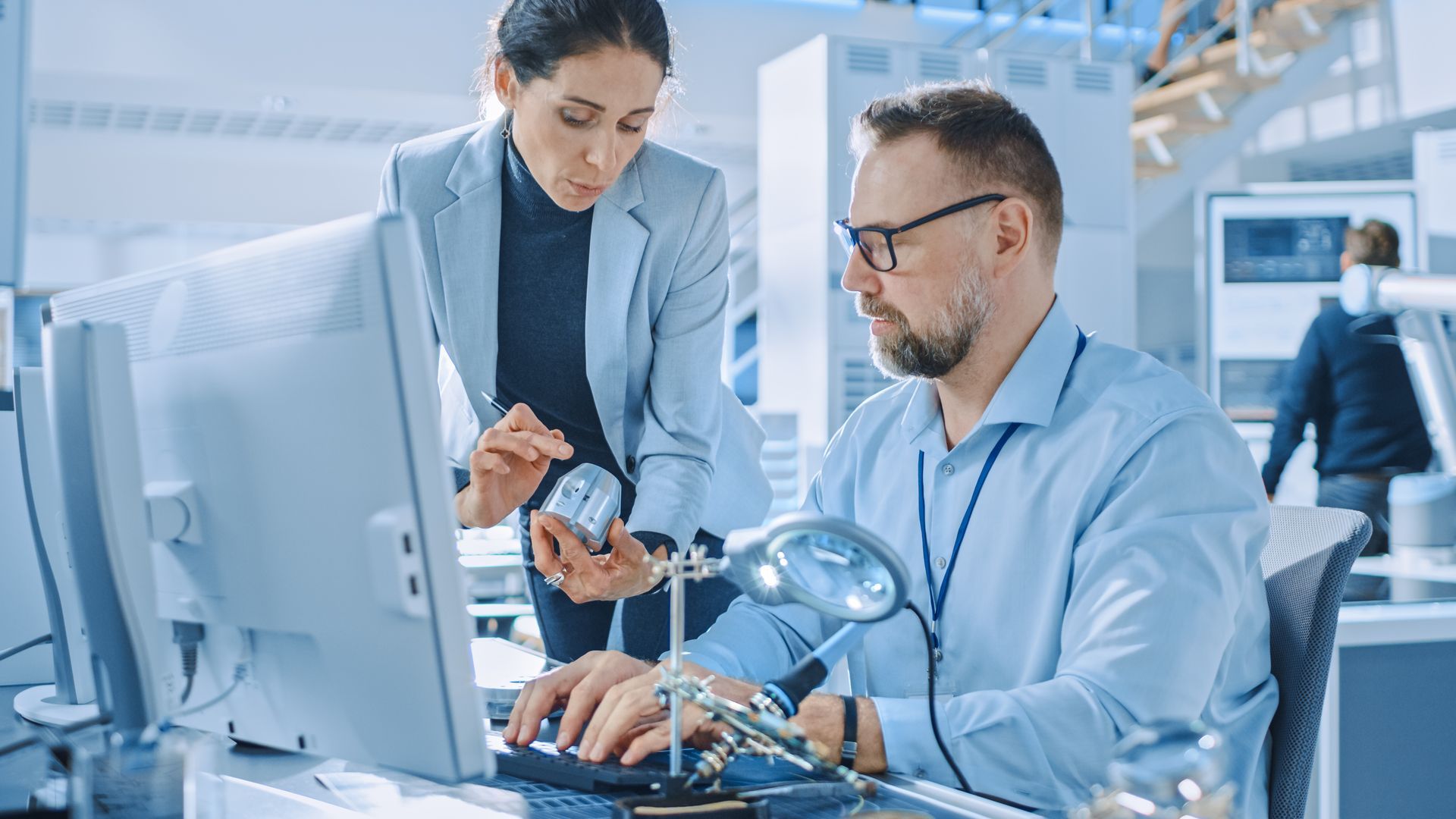 Two engineers collaborating at a workstation in a bright office, analyzing data on multiple monitors.