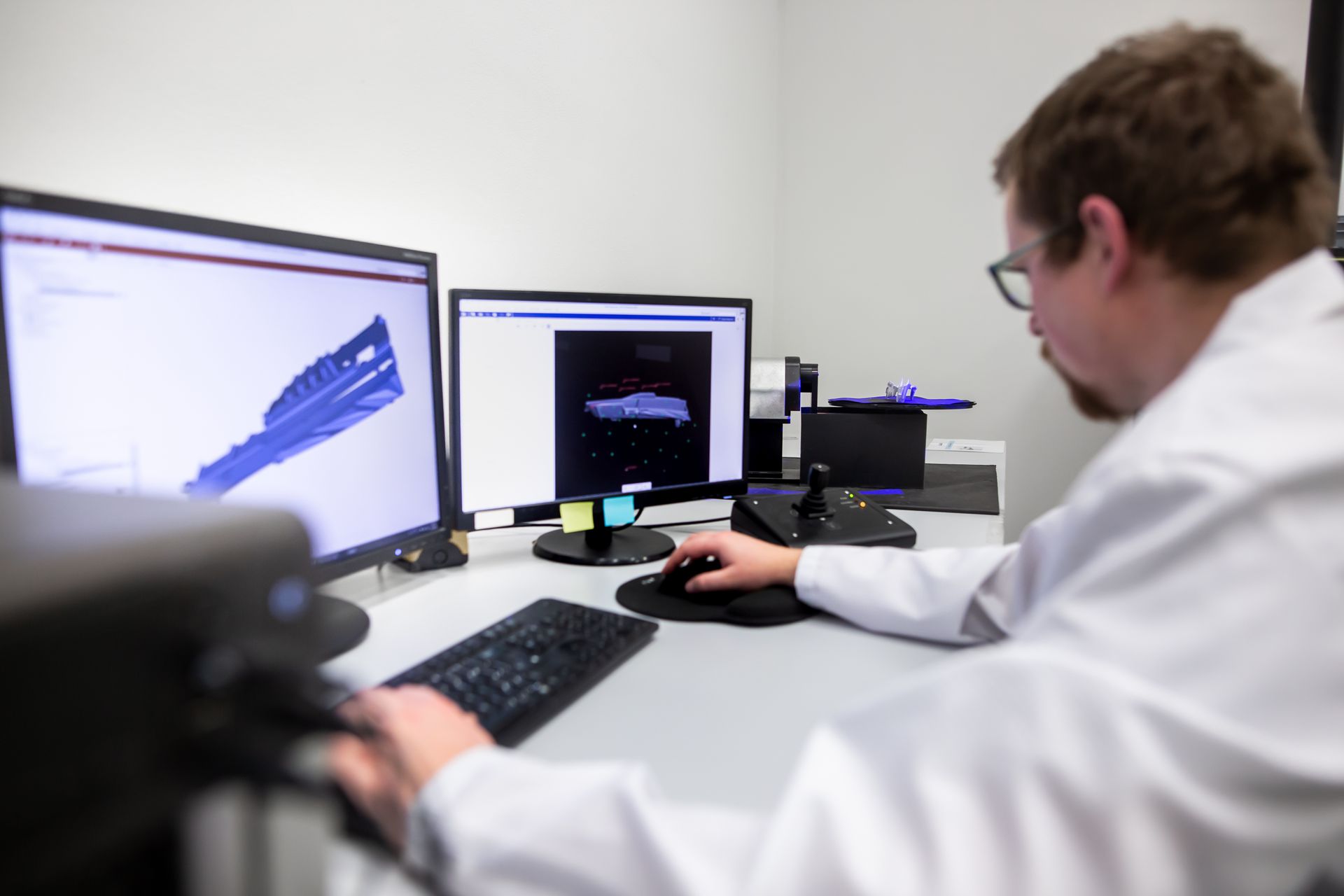 Scientist working at a desk with dual monitors displaying data graphs and code