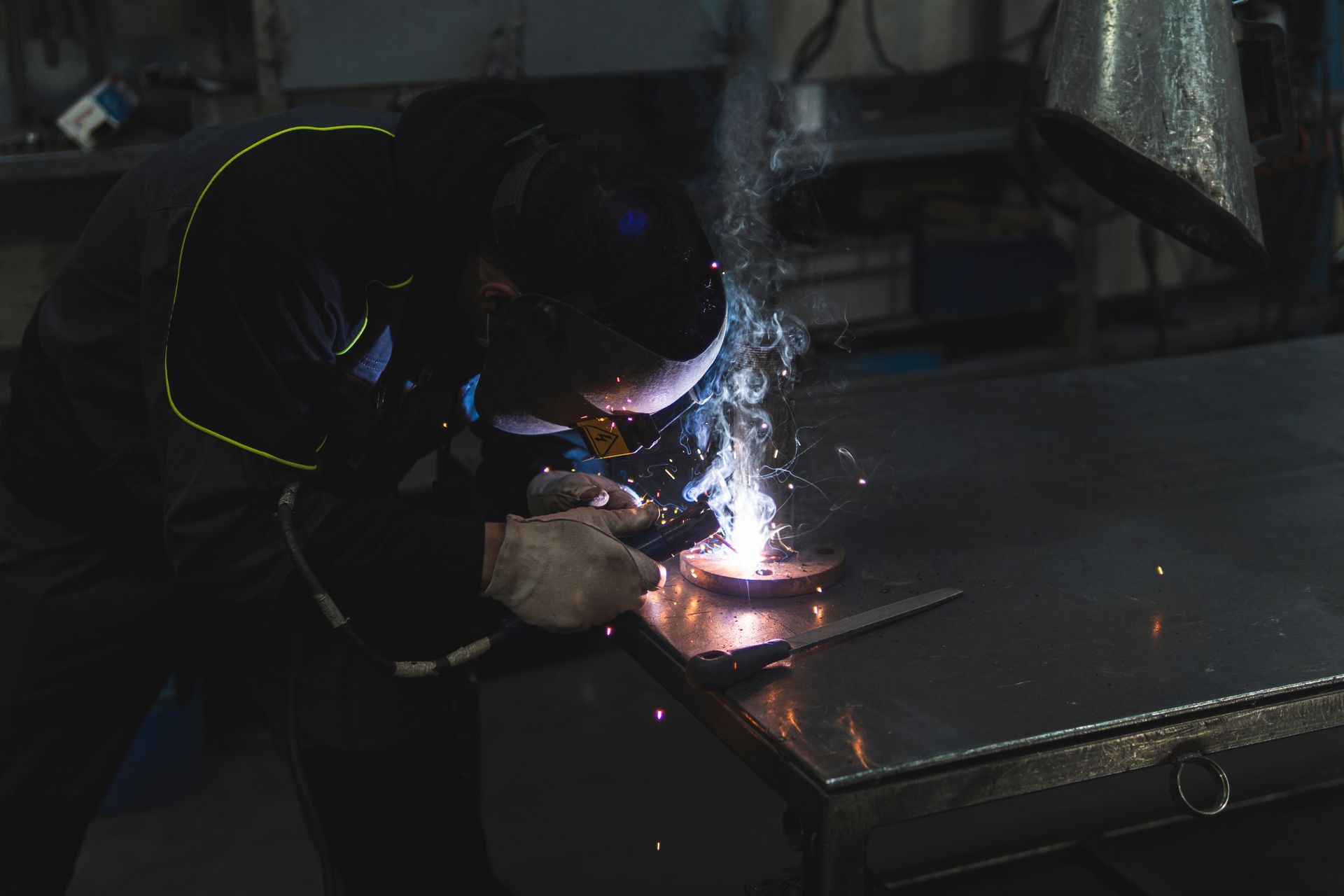 Worker welding metal on a table, with bright sparks in a dark workshop