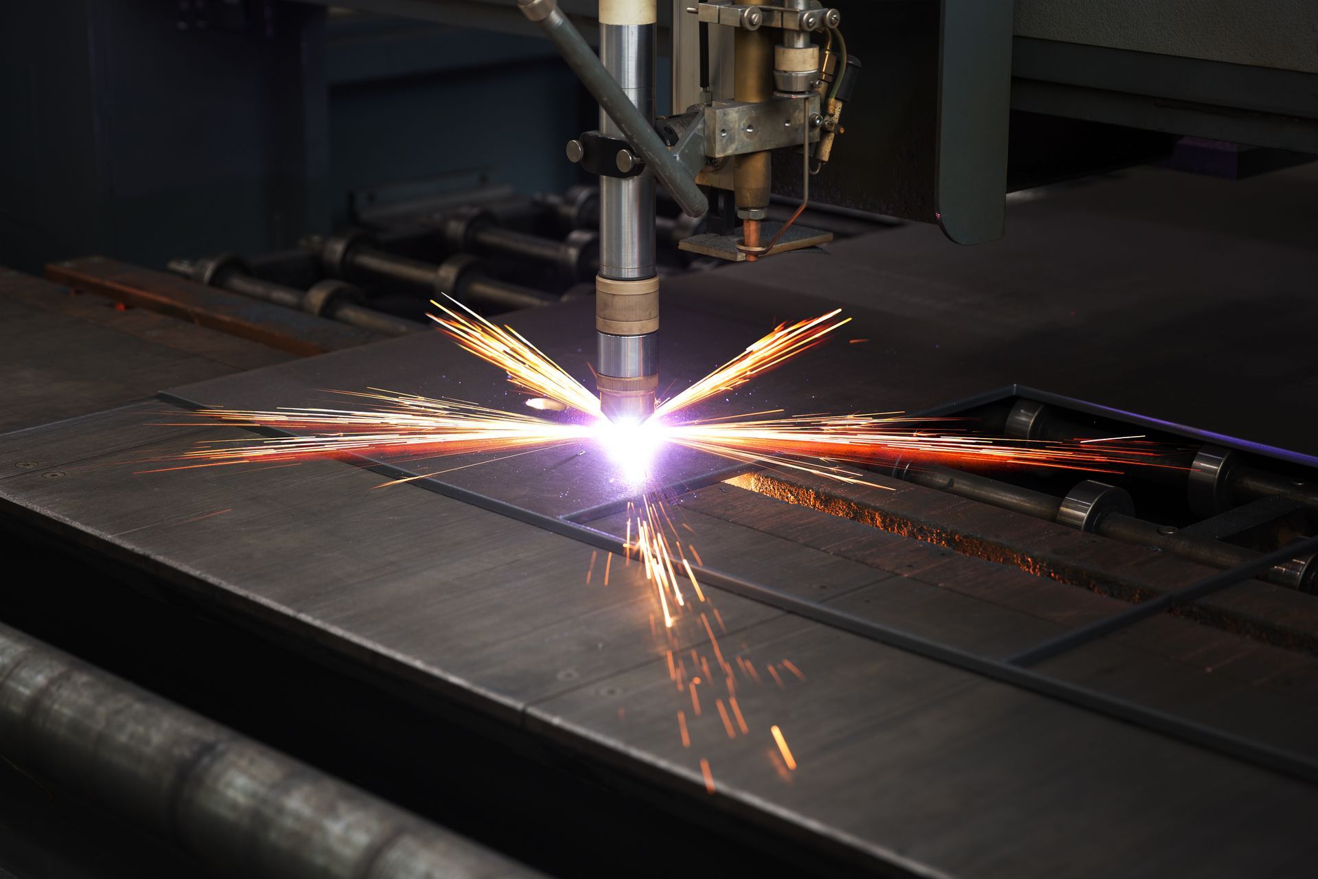 Metal-cutting laser machine spraying bright sparks on a dark workshop surface