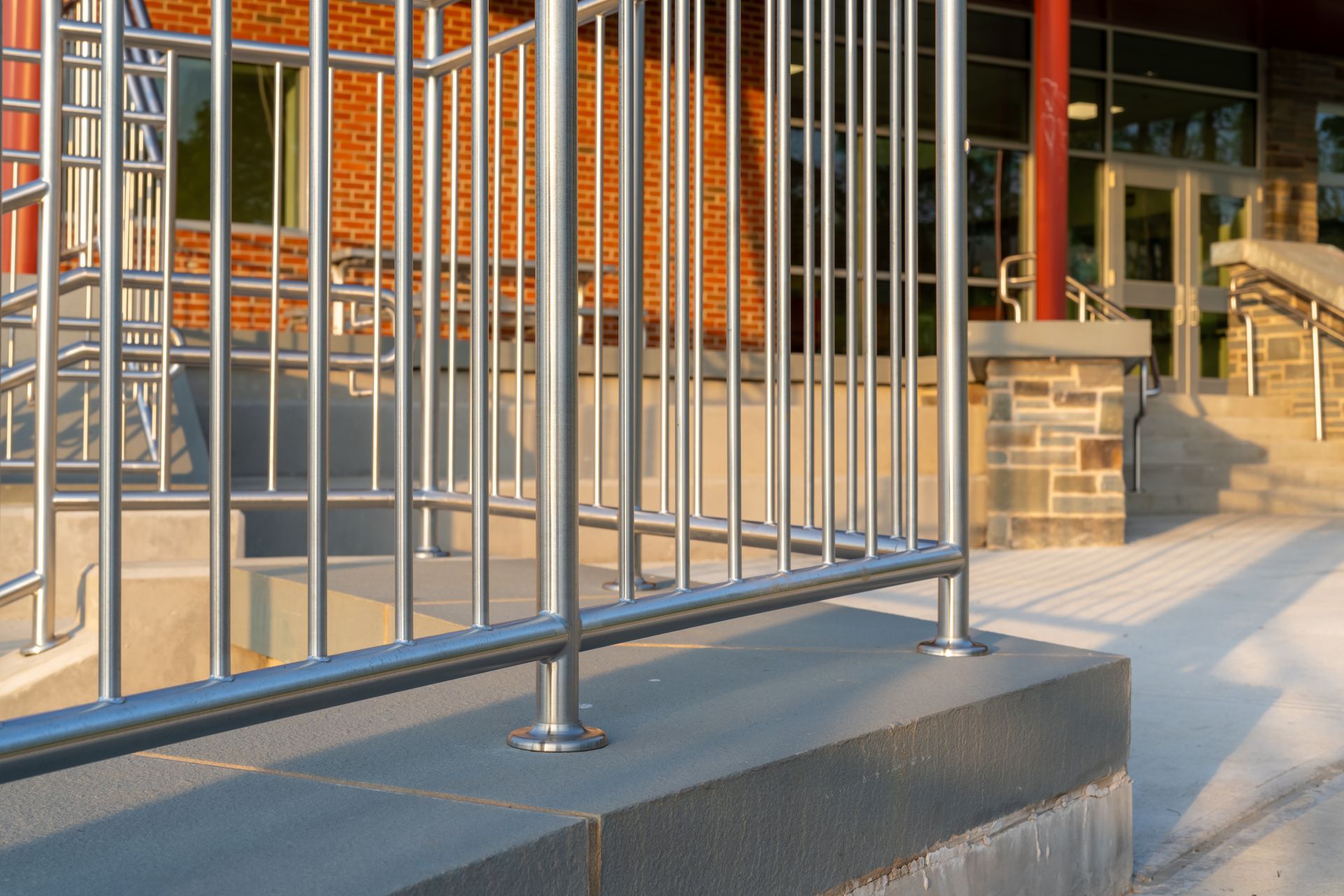 Metal railing beside brick steps and a concrete sidewalk outside a building