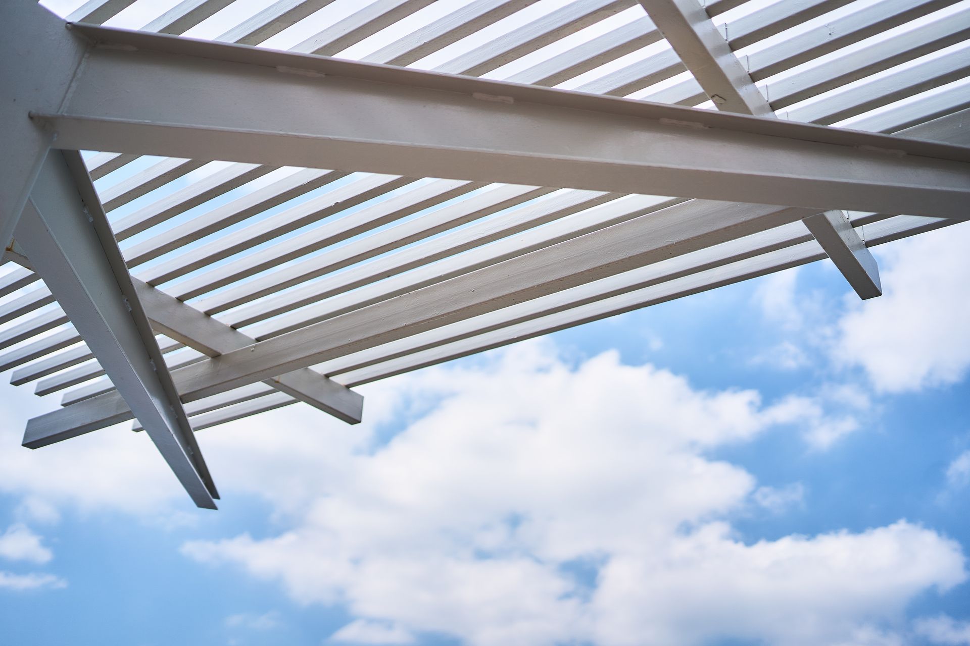 White pergola beams against a bright blue sky with clouds