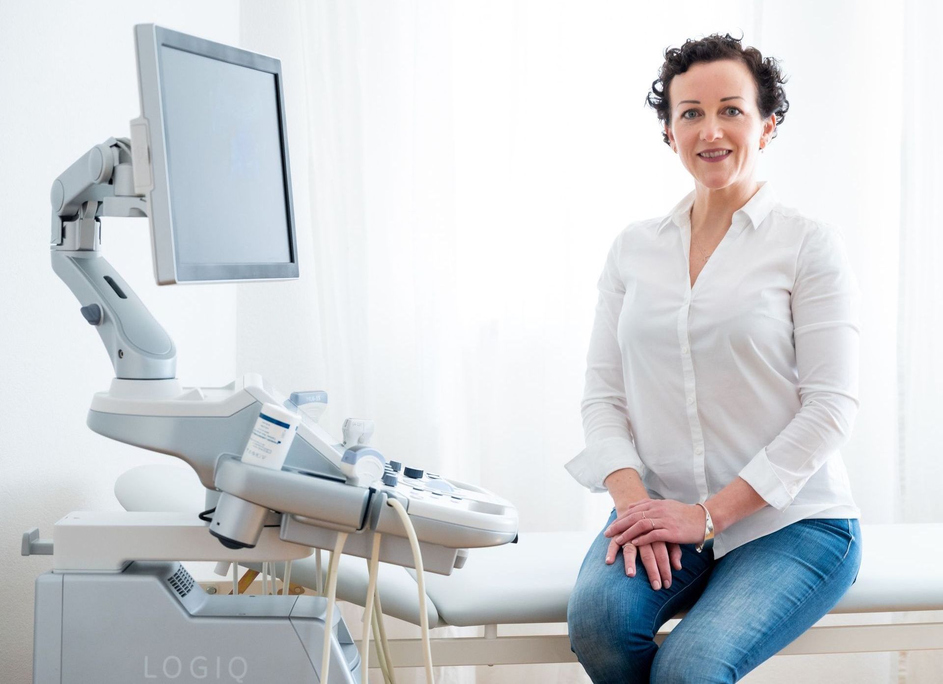 Dr. Sonja Lattenmayer-Meizer sitzt auf einem Bett vor einem Ultraschallgerät.