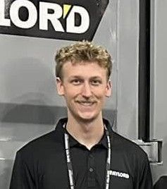 A young man wearing a black shirt and a lanyard is smiling for the camera.