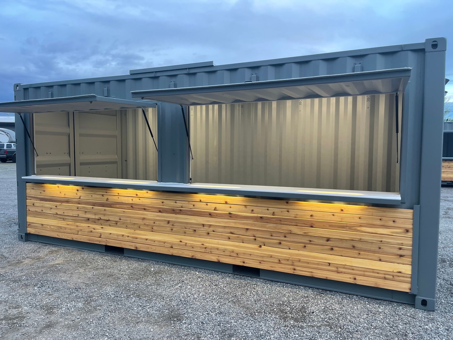 A container with a wooden counter and lights on it is sitting on top of a gravel lot.