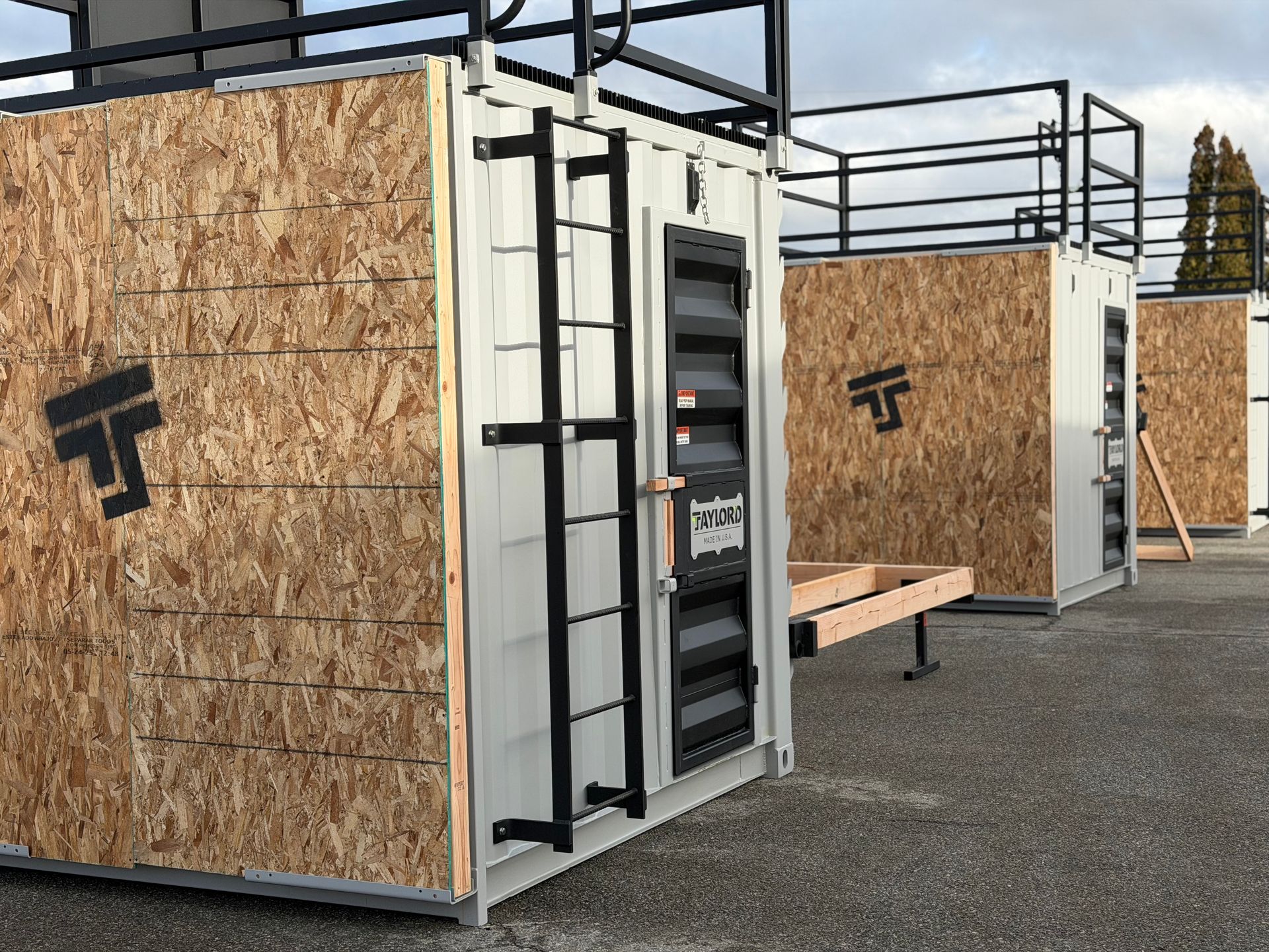 Shipping containers modified with wooden siding, ladders, and roof access.