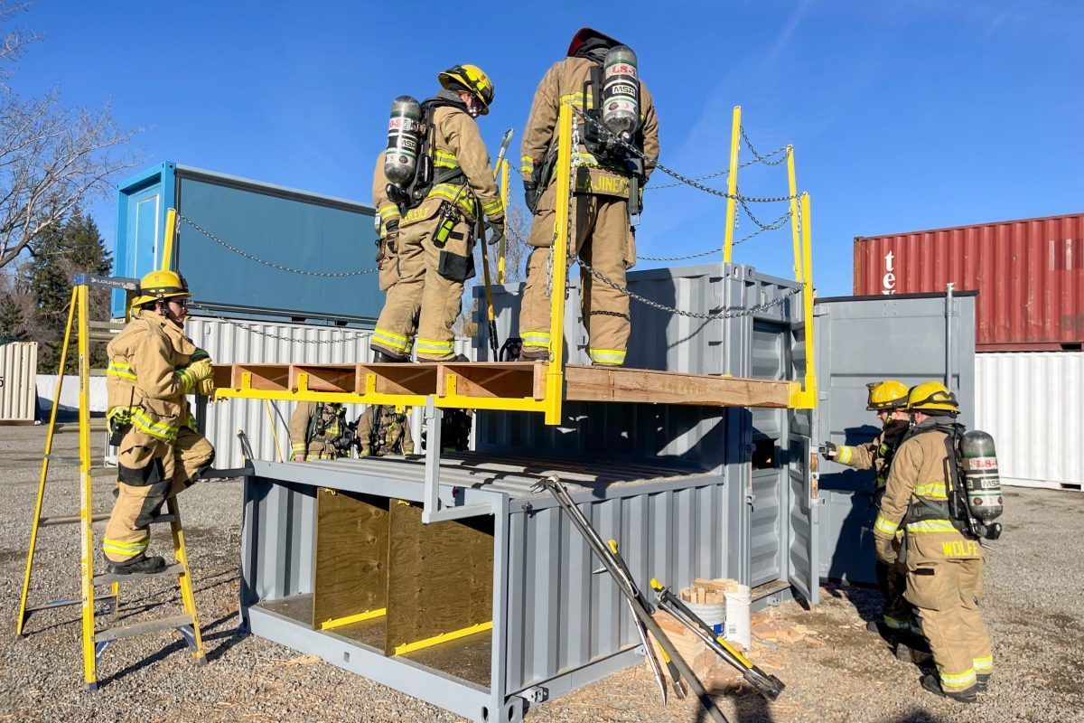 A group of firefighters are standing on top of a shipping container.