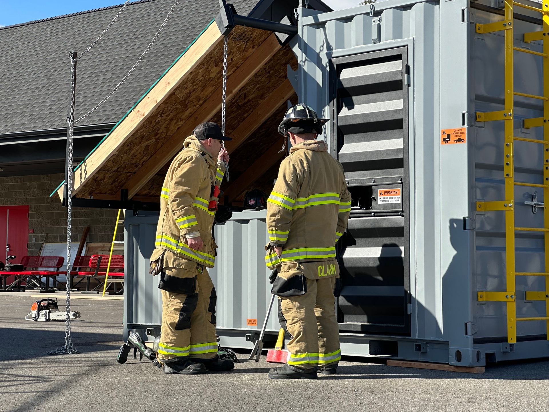 Two firefighters are standing next to each other in front of a building.