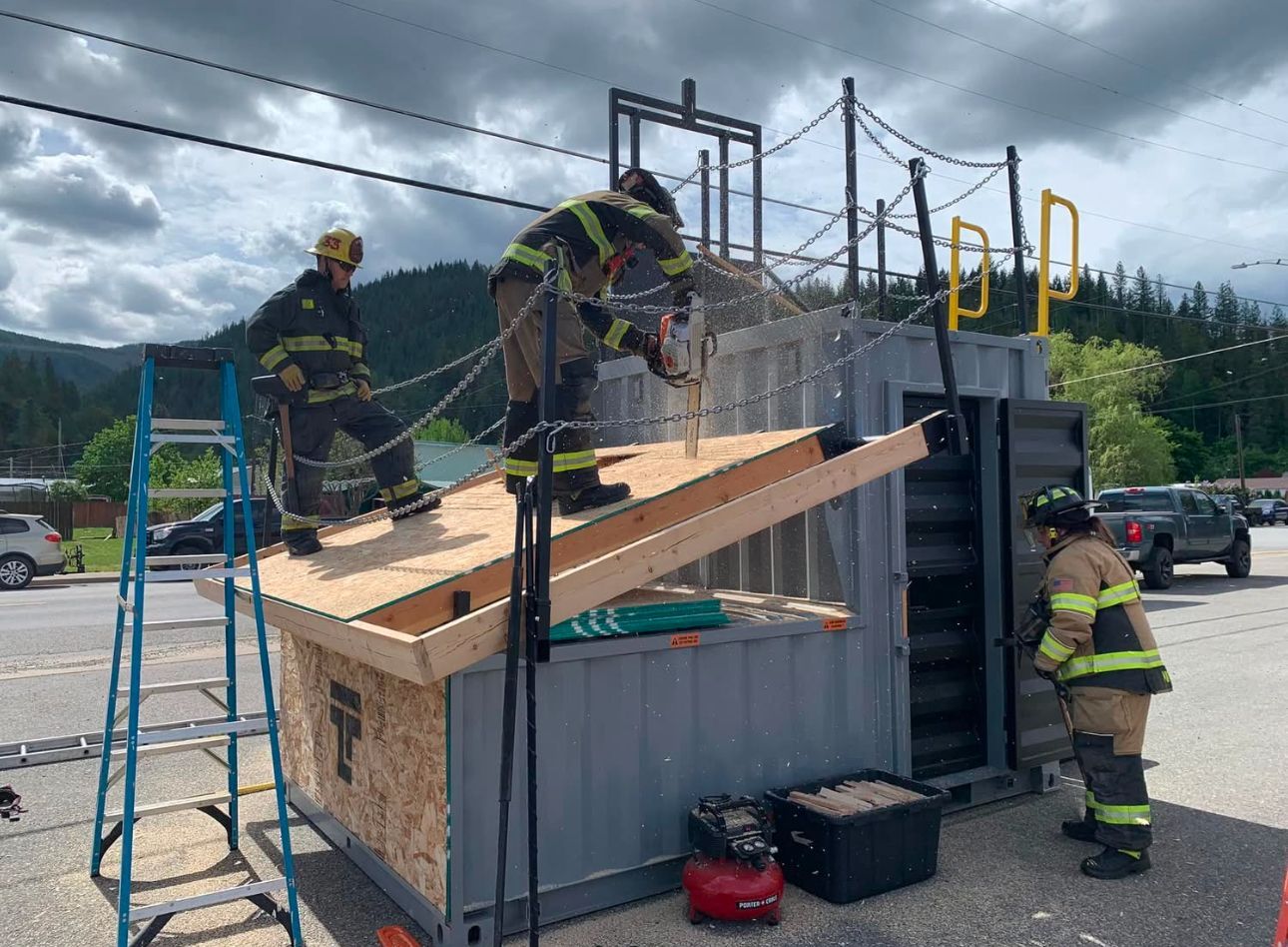 A group of firefighters are working on a roof of a shipping container.