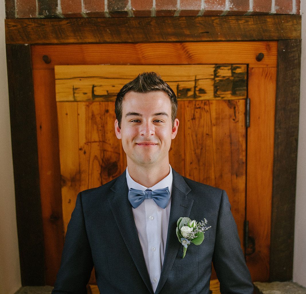 A man in a suit and bow tie is smiling in front of a wooden door
