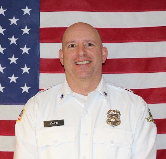 A man in a uniform is smiling in front of an american flag