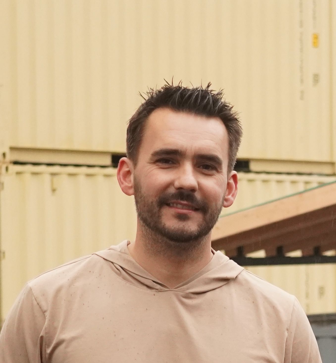 A man with a beard is wearing a tan hoodie