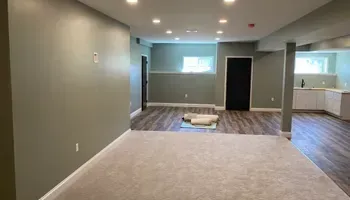 An empty basement with a carpeted floor and a kitchen.