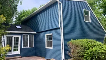 A blue house with white trim and windows is surrounded by trees.