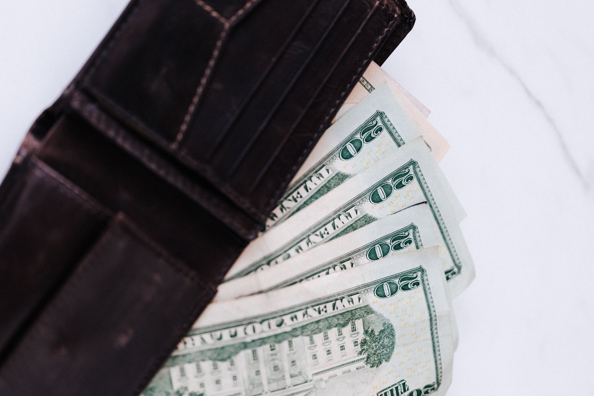 Open brown leather wallet filled with several US twenty dollar bills, on a white surface.