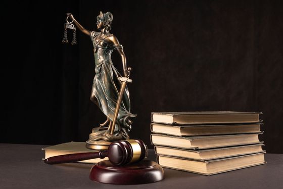 Statue of Lady Justice holding scales and sword with gavel and books in front of a dark backdrop.