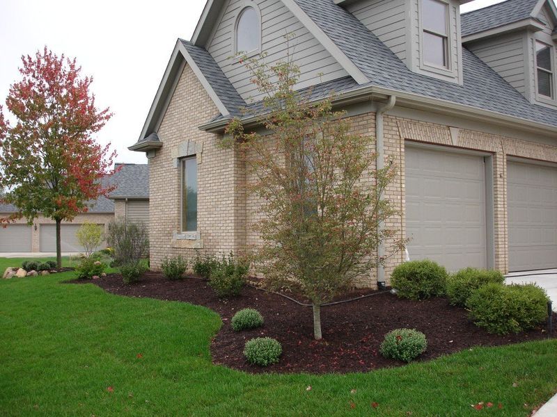 A brick house with two-car garage, manicured lawn, and colorful trees in the fall.