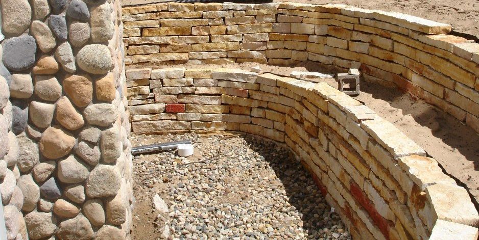 Stone retaining walls, constructed with rounded river rocks and rectangular blocks, enclose a landscaped area.