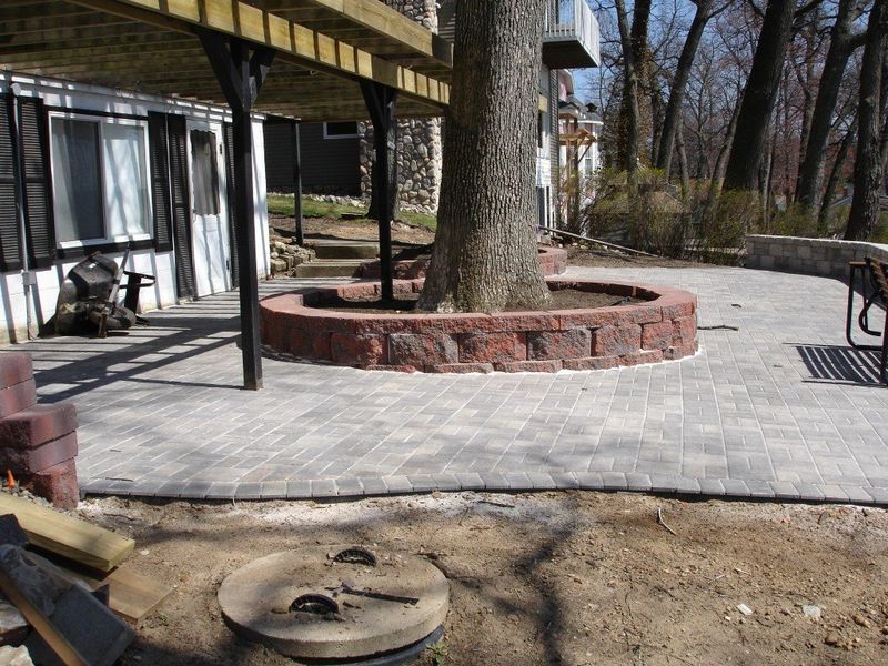 Brick patio surrounding a tree, under a deck.
