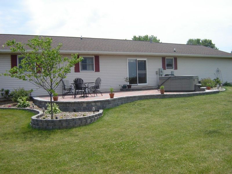 Backyard patio with a hot tub, seating, and landscaping against a beige house with a sliding glass door.