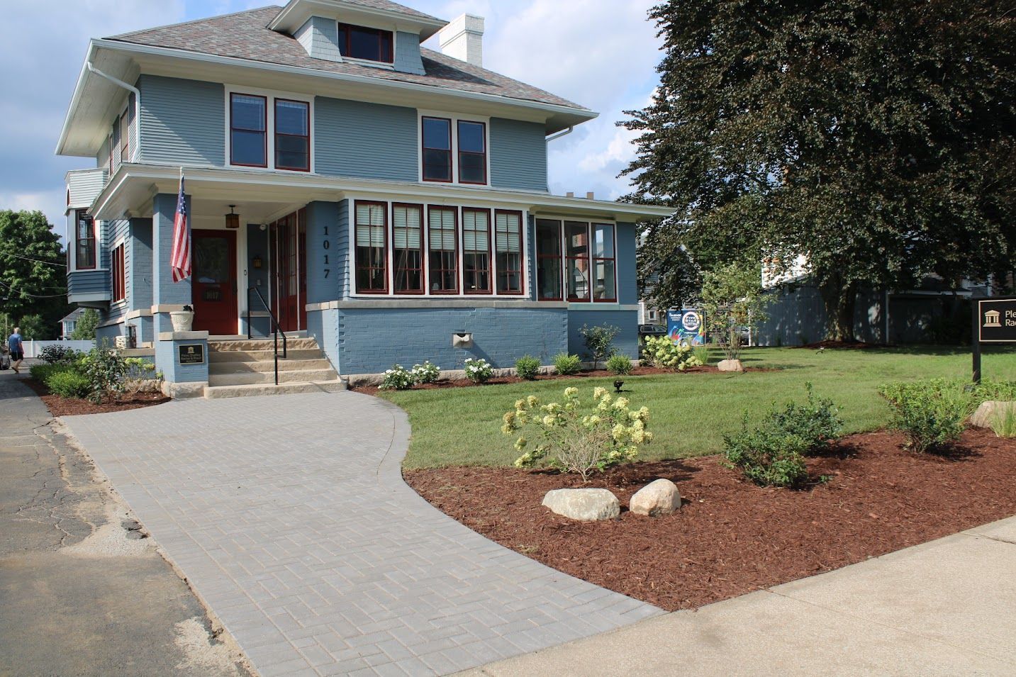 Blue house with covered porch, curved paved walkway, and landscaped yard.