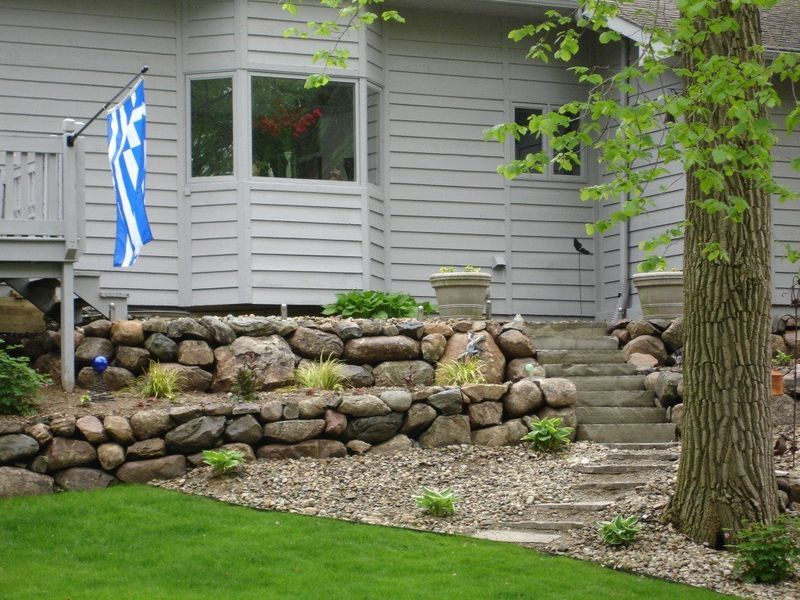 A house with a stone retaining wall, steps, and a Greek flag.